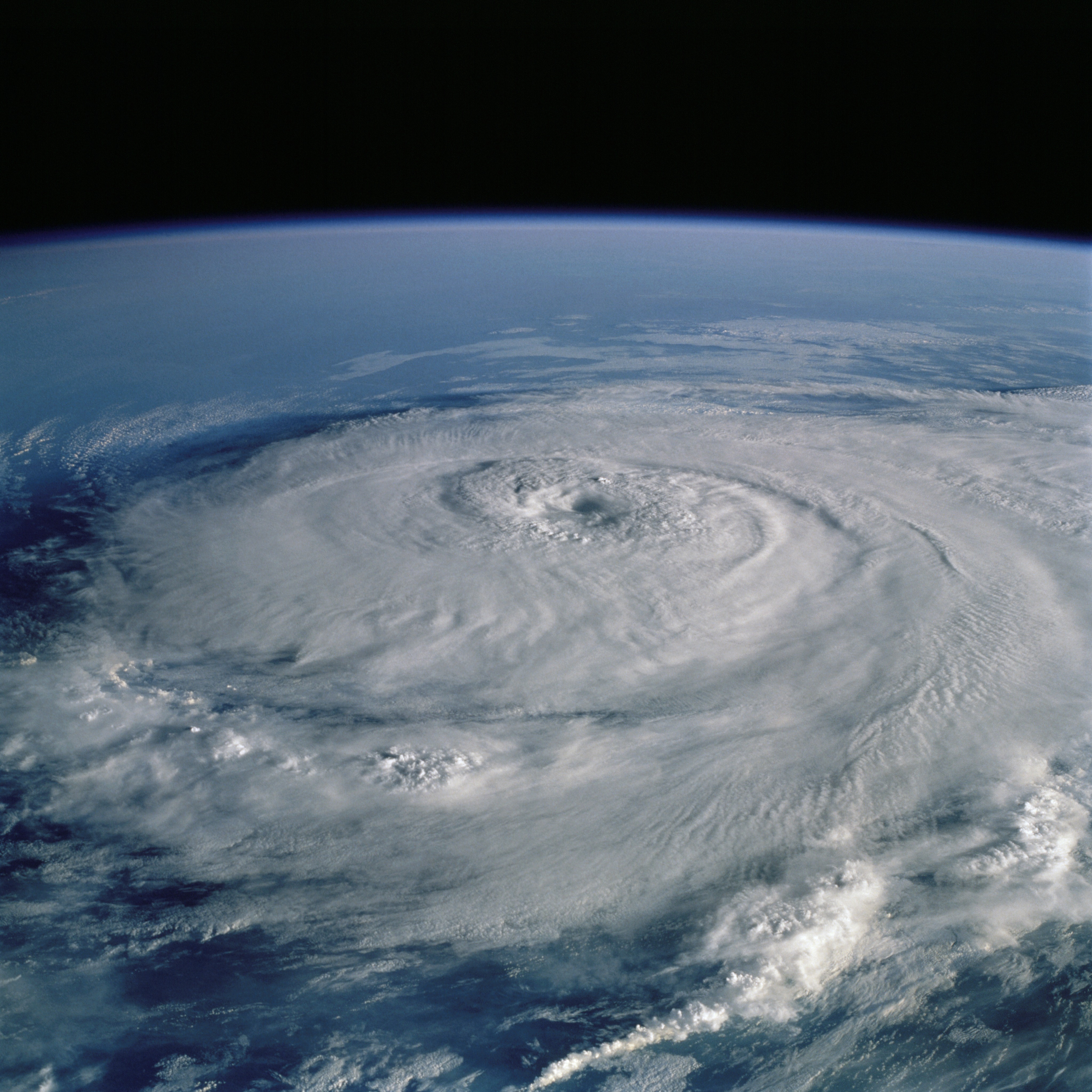 Aerial image of a hurricane from space, with white swirling clouds over a blue ocean.
