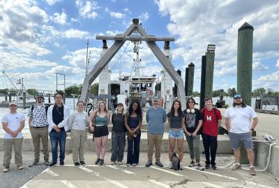 Students posing for photo on the dock in front of a ship