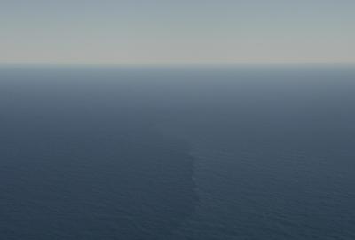 Aerial view of open ocean with a faint vertical streak marking a surface front amid calm blue water.