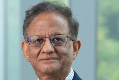 A headshot of a middle-aged man with glasses and a navy blue blazer against a soft, out-of-focus background.