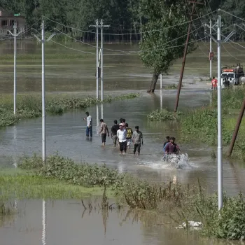 A group of people wading through a flooded road in Kashmir.