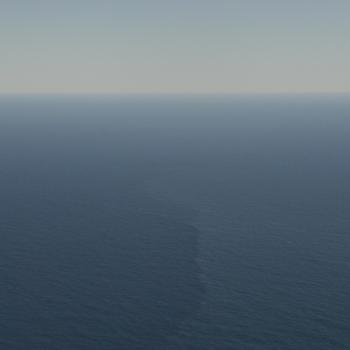 Aerial view of open ocean with a faint vertical streak marking a surface front amid calm blue water.