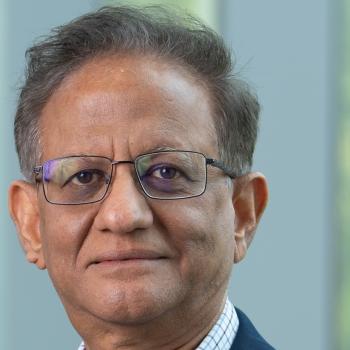 A headshot of a middle-aged man with glasses and a navy blue blazer against a soft, out-of-focus background.