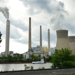 Steam rises from cooling towers at the coal-fired John E. Amos Power Plant in West Virginia on the Kanawha River as pollution from smoke stacks rises into a cloudy sky. 