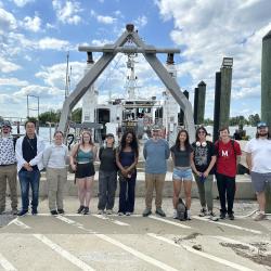 Students posing for photo on the dock in front of a ship